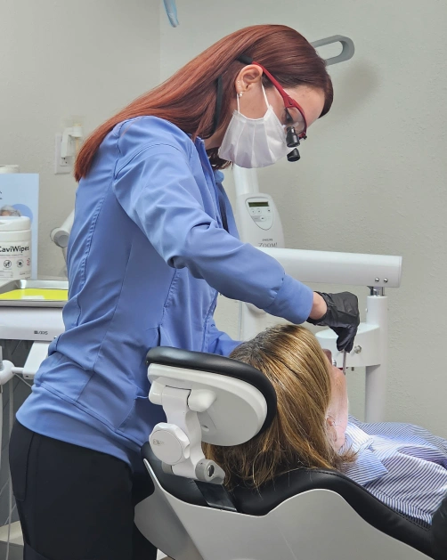 Dental hygienist in blue scrubs and mask examining a patient's teeth in a treatment chair at Wellen Family Dental in North Port, FL