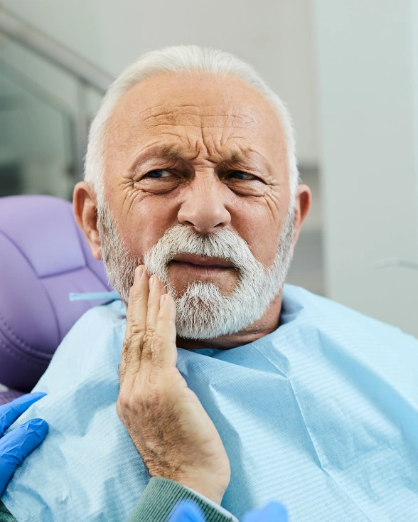 Older man holding his cheek in pain, seated in a dental chair before a tooth extraction procedure